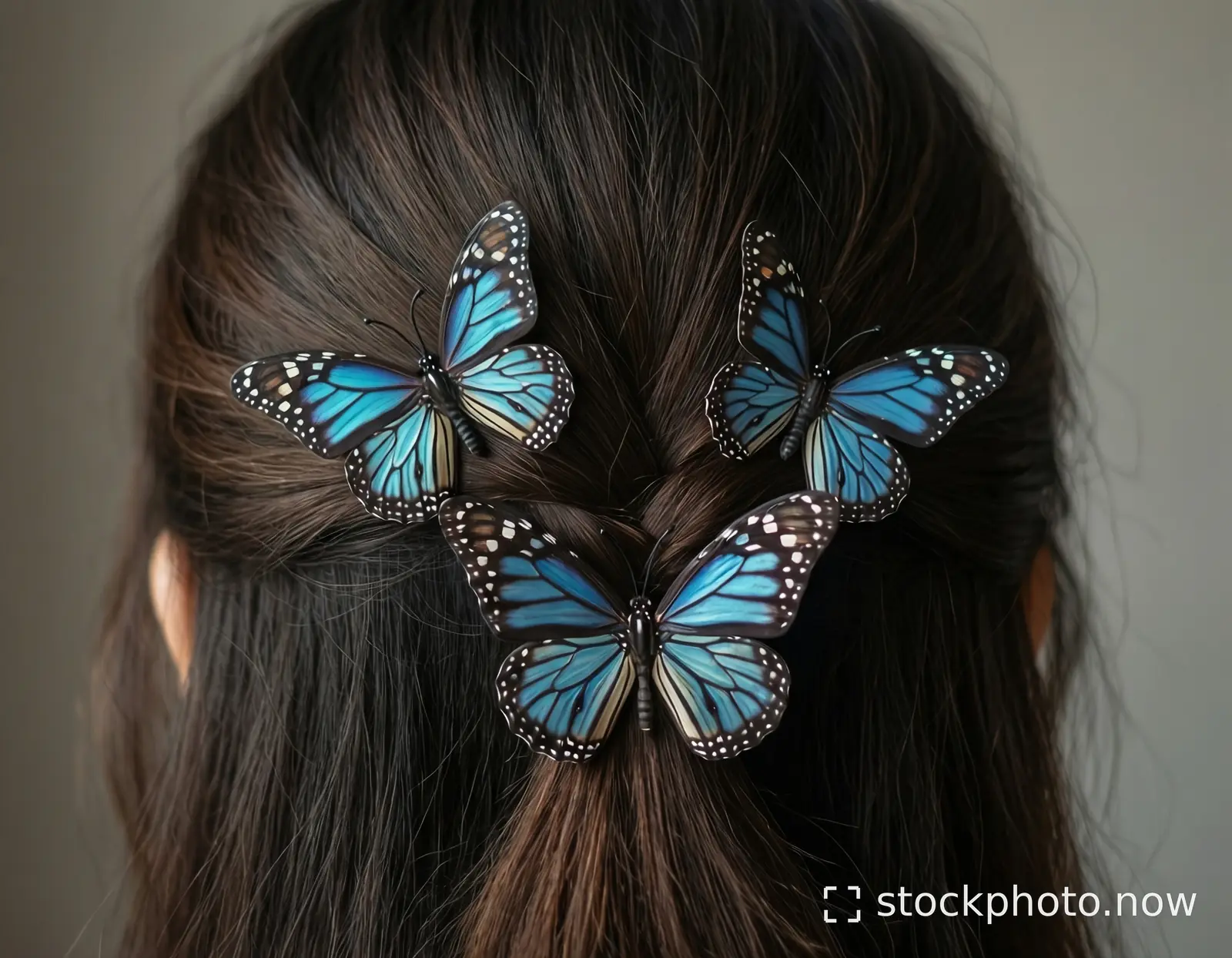 Three blue monarch butterflies with black veins rest delicately in dark brown hair tied in a low bun.