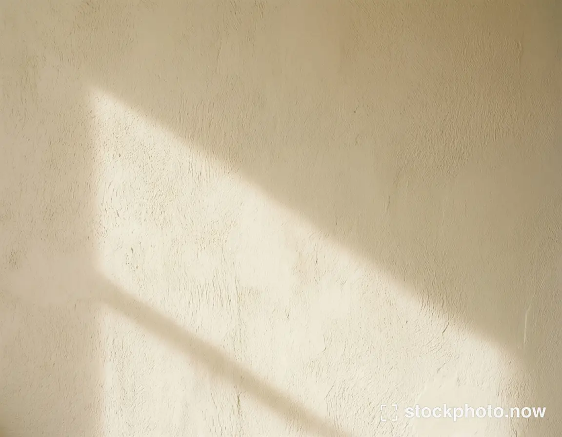 Soft diagonal sunlight and shadow falling across a lightly textured ivory wall