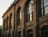 A historic red brick building with arched windows bathed in warm golden hour sunlight.