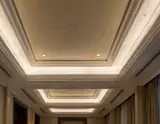 Elegant hotel hallway ceiling with layered crown molding recessed lighting and beige walls.
