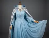 A pale blue flowing fantasy gown displayed with a shiny silver cape in a gray studio