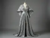 A metallic silver gown with angular sleeves and long draped folds displayed on a dress form