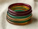 A stack of translucent red, green and amber glass bangles resting on cream linen