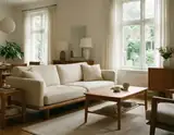 A bright airy living room with a beige sofa wooden coffee table and large windows letting in natural light.