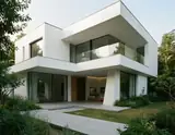 A modern white house with clean lines and glass balconies stands amidst lush greenery under a soft sky.