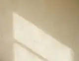 Soft diagonal sunlight and shadow falling across a lightly textured ivory wall