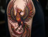 A vividly colored phoenix tattoo with fiery orange red and yellow feathers spreads across a person's upper arm.