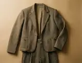 A brown patterned blazer laid over matching trousers on a warm beige background
