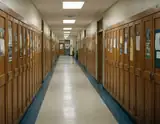Long empty school hallway lined with wooden lockers and fluorescent lights overhead.