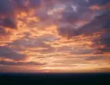 Layers of glowing peach and lavender clouds above a dark distant horizon