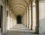 A centered view along repeating pale stone arches and columns with alternating light and shadow