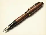 A finely detailed vintage fountain pen with dark wood barrel and gold trim rests diagonally on a cream background.