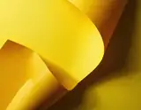 Overlapping bright yellow paper curves creating deep warm shadows in an abstract composition