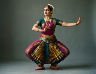 An adult classical Indian dancer in a colorful traditional costume holding a poised studio dance position
