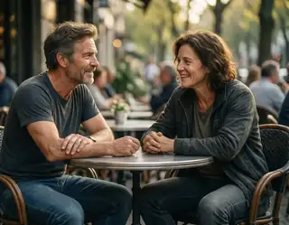 A middle-aged couple shares a warm smile across a café table as golden afternoon light filters through trees behind them.
