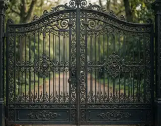 An ornate black wrought iron gate with intricate scrollwork stands open revealing a sunlit forest path beyond.