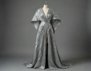 A metallic silver gown with angular sleeves and long draped folds displayed on a dress form