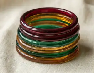 A stack of translucent red, green and amber glass bangles resting on cream linen
