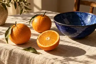 Fresh oranges and a cobalt blue ceramic bowl on a cream tablecloth
