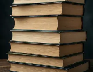 A tall stack of vintage hardcover books with worn beige pages and dark green spines stands against a deep black background.
