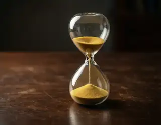 A glass hourglass filled with golden sand on a dark wooden tabletop