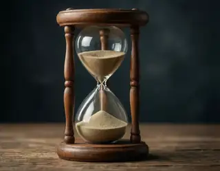 An antique wooden hourglass with amber sand rests on a rustic table against a dark backdrop.