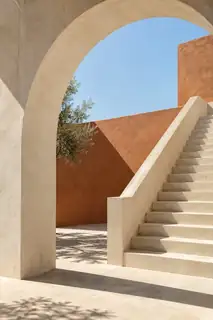 Cream concrete arch and staircase beside a terracotta wall in sunlight