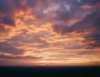 Layers of glowing peach and lavender clouds above a dark distant horizon