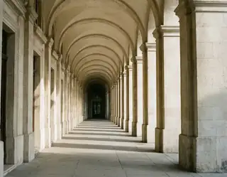 A centered view along repeating pale stone arches and columns with alternating light and shadow