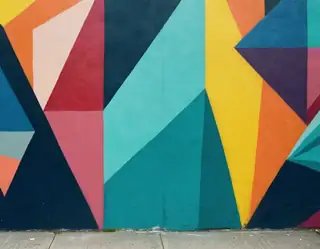 Vibrant geometric mural with bold triangles in teal yellow red and navy painted on a concrete wall.
