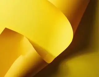 Overlapping bright yellow paper curves creating deep warm shadows in an abstract composition